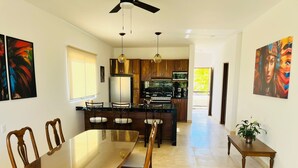 A modern kitchen with wooden cabinets, a central island, and a dining area with a glass-top table and wooden chairs.