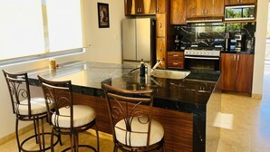 A modern kitchen with wooden cabinets, a large island with bar stools, stainless steel appliances, and pendant lighting.