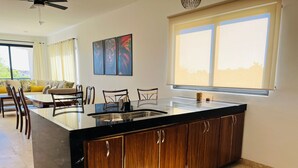 A modern kitchen with a large island, wooden cabinets, and a large window providing natural light.
