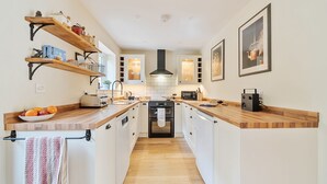 A modern kitchen with wooden countertops, white cabinets, and a central island. There are built-in shelves above the countertops and a microwave on the right side.