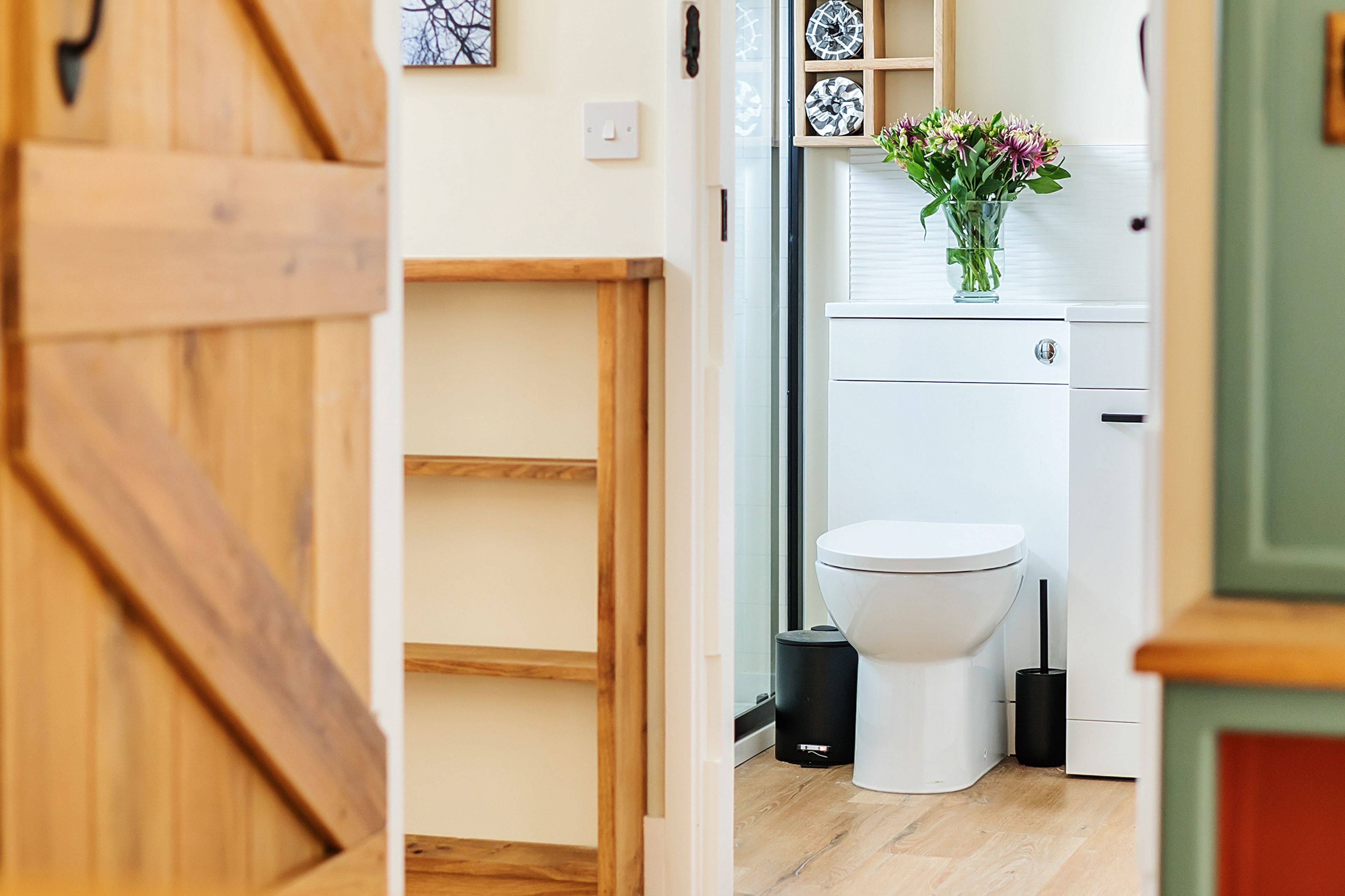 Un baño moderno con inodoro, un bote de basura negro y un florero con flores sobre el lavamanos.