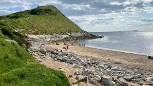 A beach with a grassy hill, rocky shoreline, and people enjoying the area.