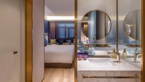 Une chambre d’hôtel moderne avec un grand lit, une salle de bain dotée d’un miroir rond et un comptoir en marbre.