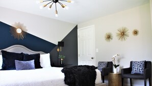 A bedroom with a bed, bedside tables, a lamp, decorative wall art, and a chair. - Charming 3-bedroom ranch home, back deck, close to ATL, in peaceful Norcross (Norcross)