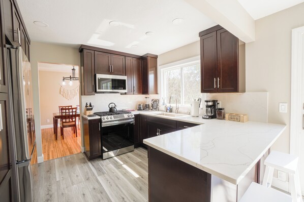 A modern kitchen with dark wooden cabinets, a large island, stainless steel appliances, and a dining area with a wooden table and chairs.