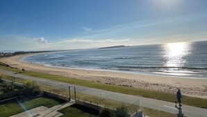 Uitzicht op de kust met een verharde promenade, strand en zee.