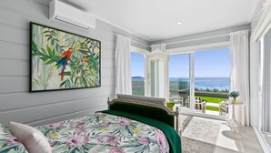 Een slaapkamer met een bed, een schilderij van papegaaien, uitzicht op de oceaan en een balkon met een tafel en stoelen.