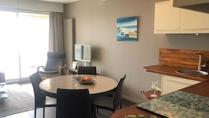Ett modernt hotellrum med en matplats, ett kök med en bänkskiva i trä och ett stort fönster med gardiner.