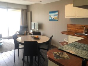 Quarto de hotel moderno com área de refeições, cozinha com bancada de madeira e uma janela grande com cortinas.