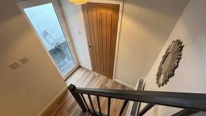 Eine Treppe mit Holzgeländer führt zu einem Raum mit einer Holztür und einem Fenster.