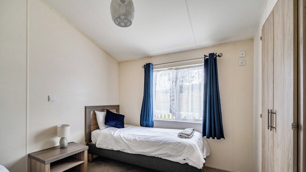 Ett sovrum med en säng, ett nattduksbord, en lampa, ett fönster med gardiner och en garderob.