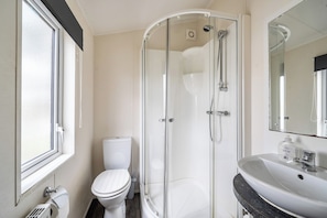 Un baño moderno con ducha de vidrio, inodoro blanco y lavamanos con encimera de mármol.