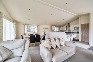 A modern living room with a sofa and chairs, a dining area with a table and chairs, and a kitchen with appliances.
