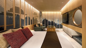 Una habitación de hotel moderna con una cama grande, un sofá, una mesita y un televisor fijado a la pared.