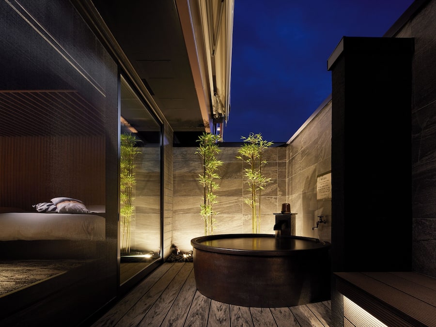 A modern bathroom with a wooden floor, a large bathtub, and a wooden bench.