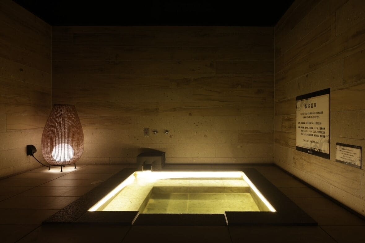 A dimly lit room with a wooden floor, a lit lamp, and a sign on the wall.