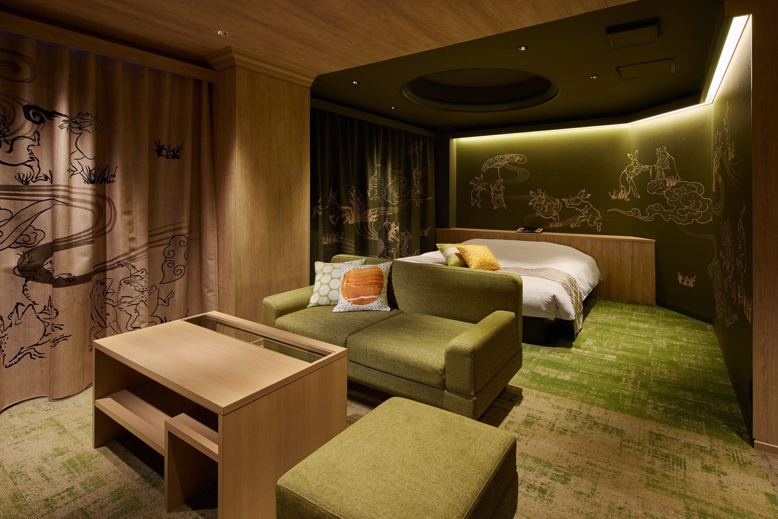A hotel room with a green sofa, a wooden table, a bed with white bedding, and a green carpet.