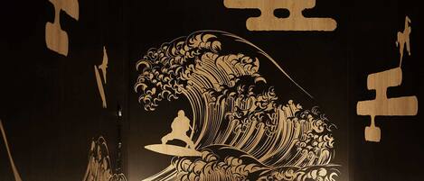 A room with a large wave painting on the wall, a ceiling vent, and a small table.