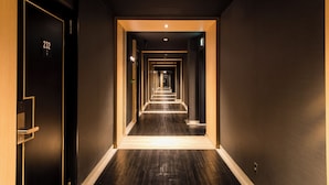 Un pasillo de hotel con piso de madera oscura, una puerta negra con el número 232 y una serie de puertas que se adentran en la distancia.