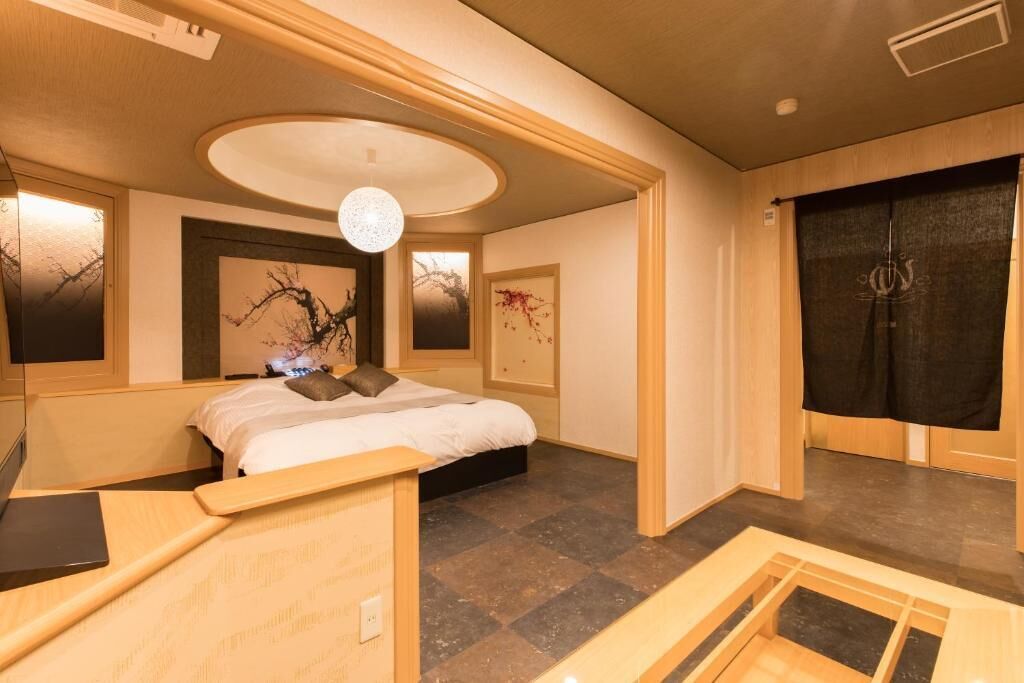 A bedroom with a bed, a desk, a chair, a round ceiling light, and artwork on the walls.