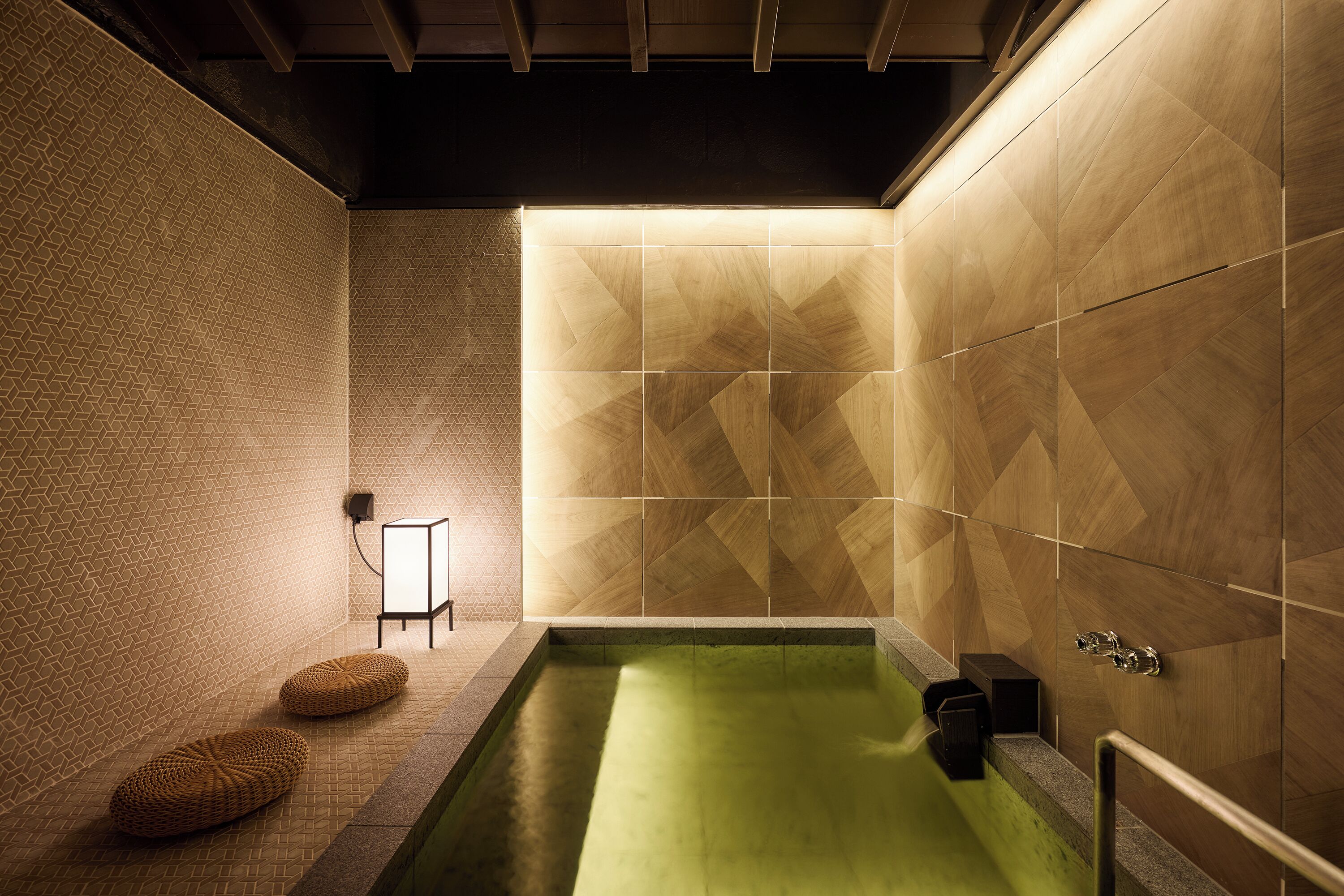 Ein modernes Badezimmer mit geometrischem Fliesendesign, ein grün gefliestes Schwimmbecken und eine Holzbank.