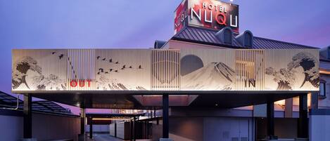 A hotel with a prominent sign, a covered entrance, and a facade featuring traditional Japanese artwork.
