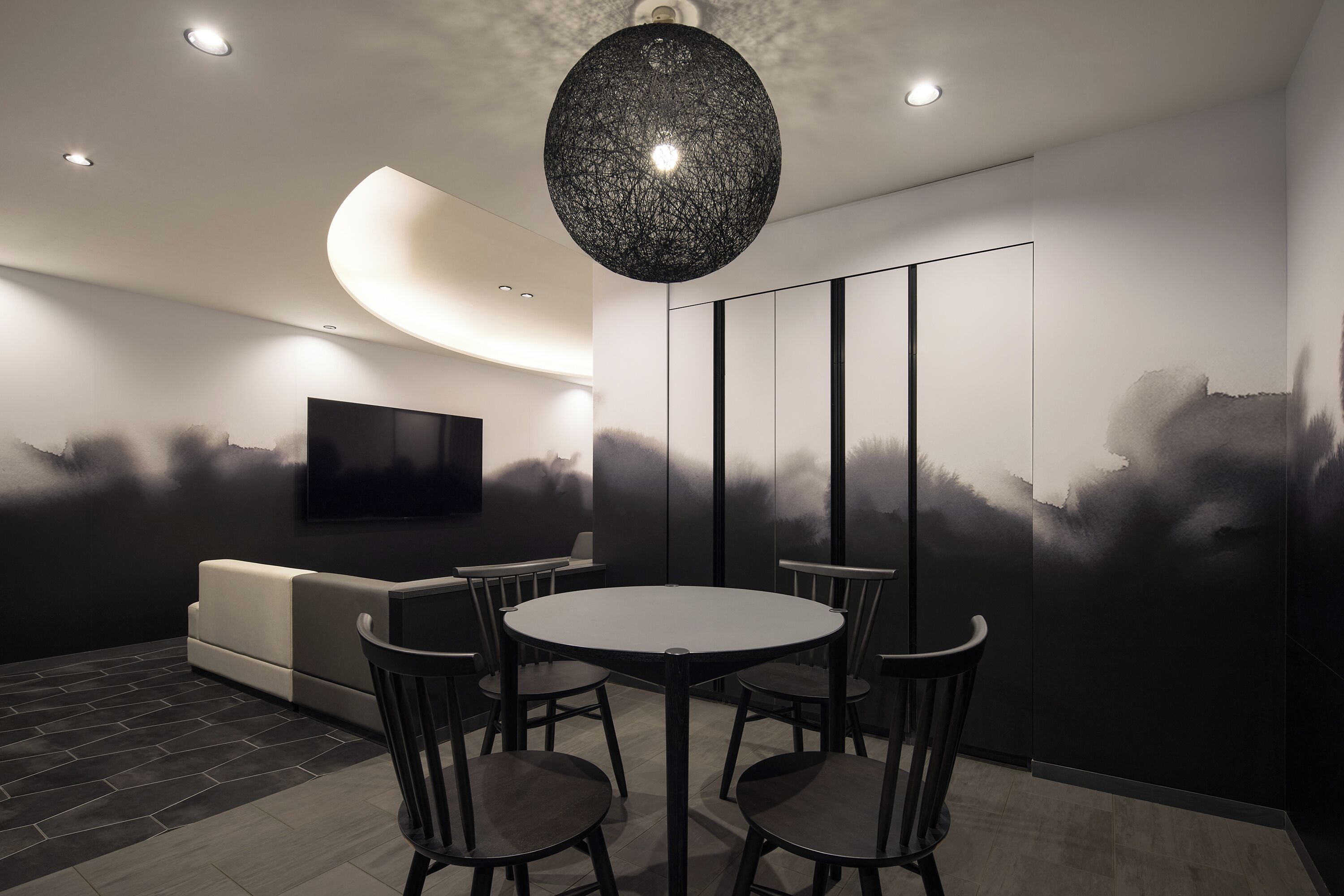 A modern dining area with a round table and four chairs, a sofa, and a wall-mounted TV.