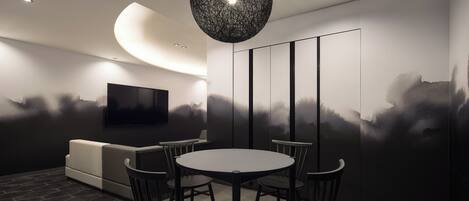 A modern dining area with a round table and four chairs, a sofa, and a wall-mounted TV.