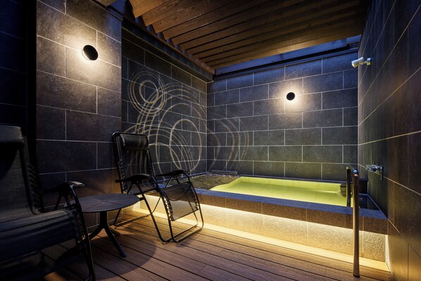 Une salle de bain moderne avec une grande baignoire, un plancher en bois et des murs recouverts de carreaux de couleur foncée.