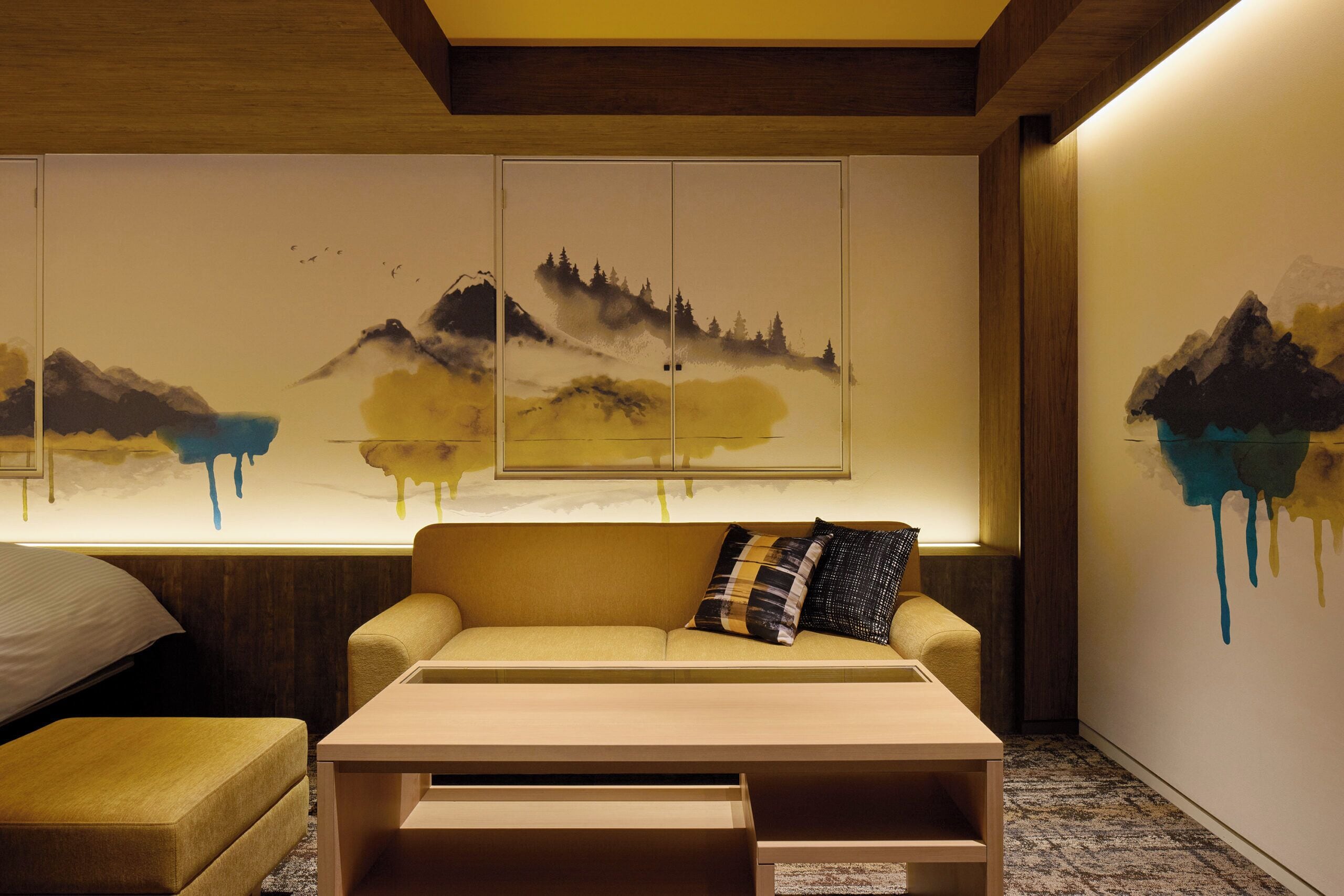 A room with a sofa, a coffee table, and a wall with abstract mountain paintings.