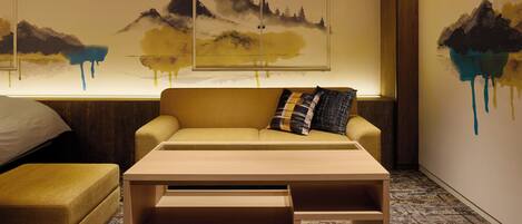 A room with a sofa, a coffee table, and a wall with abstract mountain paintings.