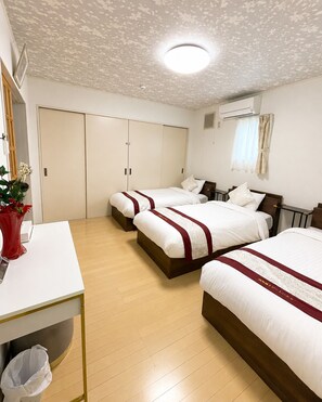 A hotel room with three beds, a white desk, a trash bin, and an air conditioning unit. - Yamanakako Resort House I (Yamanakako)