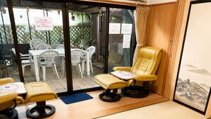 A room with tatami mats, a yellow chair, and a view of an outdoor patio with white furniture. - Yamanakako Resort House I (Yamanakako)