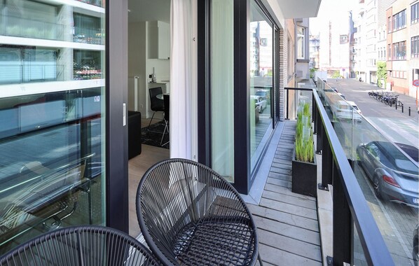 A balcony with a view of the street, a chair, and a small table with a lamp.