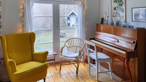 A room with a yellow armchair, a wicker chair, a piano, and a large window with curtains. - Cozy home in Vejby with WiFi (Vejby)