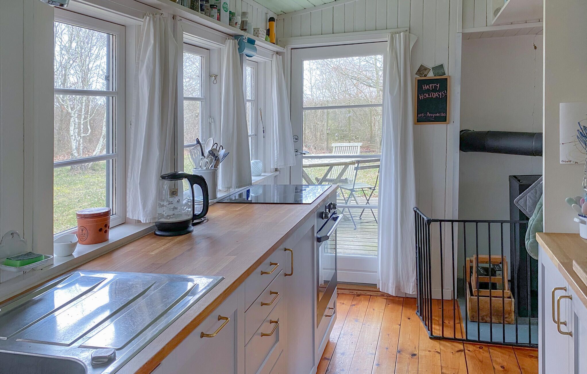 A kitchen with a wooden countertop, a kettle, and a view of the outdoors.