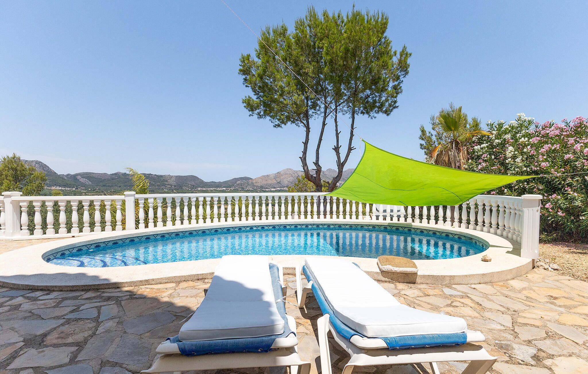 A swimming pool with a white balustrade, two lounge chairs, and a green shade sail.