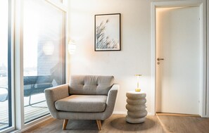 Een moderne kamer met een grijze fauteuil, een ingelijste afbeelding, een bijzondere ronde tafel en een deur.
