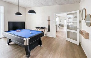 Een pooltafel met een blauwe viltkleed, twee zwarte hanglampen en een biljarthouder met stokken.