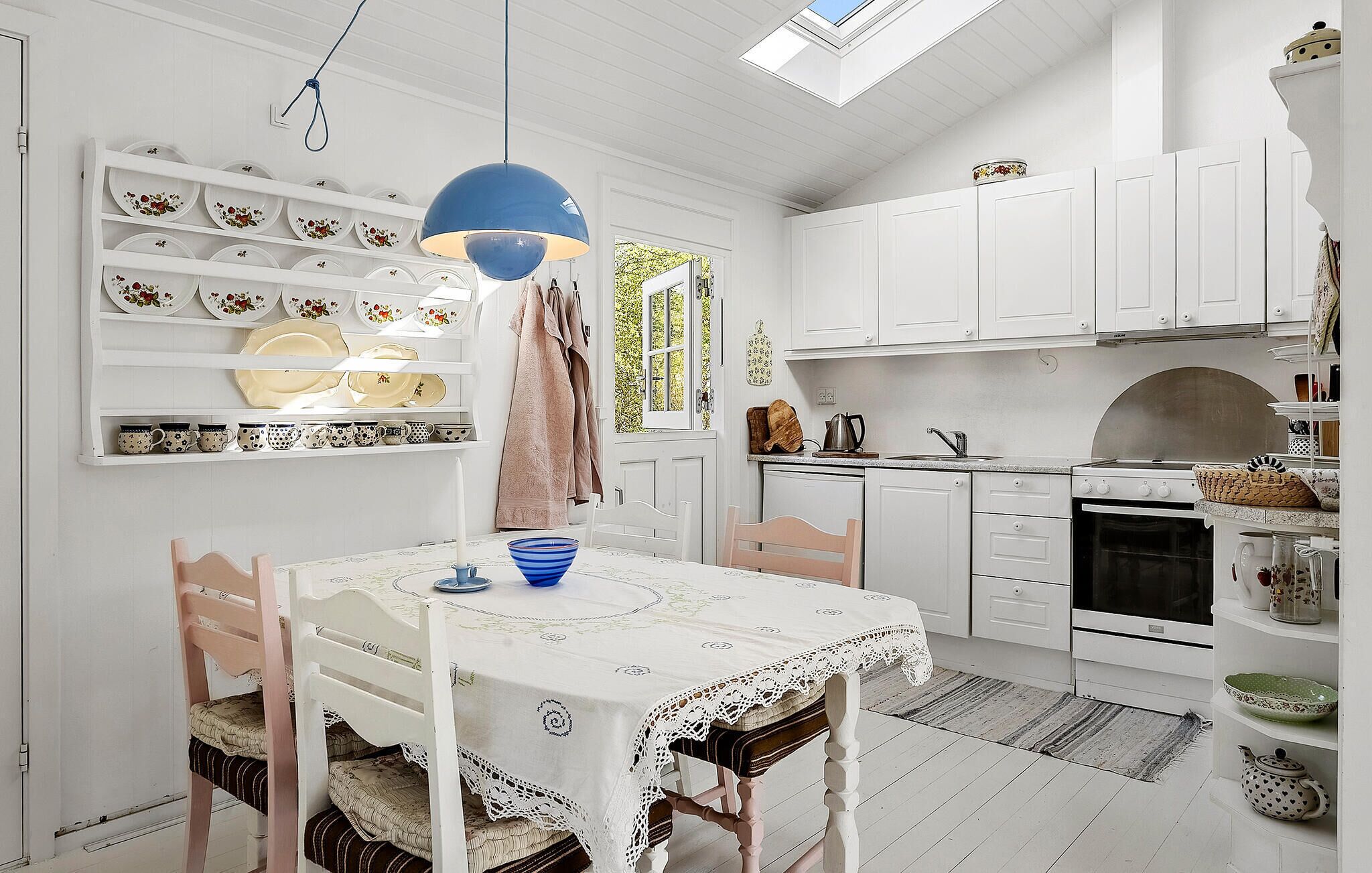 A kitchen with white cabinetry, a dining table with a lace tablecloth, and a blue pendant light.