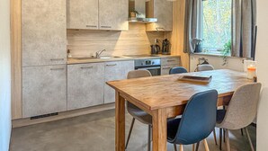 A modern kitchen with a wooden table and chairs, a built-in oven, and a window with curtains. - 3 bedroom nice home in Hoeven (Hoeven)