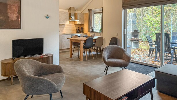 A modern living room with a TV, two armchairs, a coffee table, and a dining area with a table and chairs. - 3 bedroom nice home in Hoeven (Hoeven)