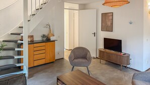 A modern living room with a staircase, a TV, and a wooden cabinet. - 3 bedroom nice home in Hoeven (Hoeven)
