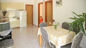 A dining area with a table set for four, a television on a stand, a refrigerator, and a kitchen in the background. - Pet friendly apartment in Hvar with WiFi (Hvar)