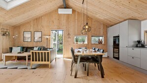 A spacious loft with a high ceiling, wooden walls, a dining area with a table and chairs, a kitchen with modern appliances, and a cozy seating area with a sofa and cushions.