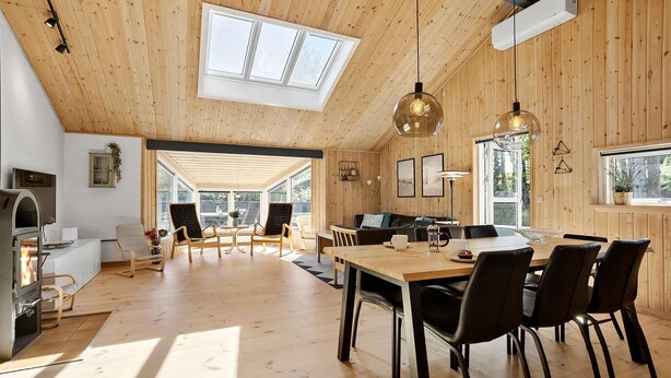 A spacious wooden interior with a high ceiling, a dining area with chairs and a table, and a kitchen with a built-in oven.