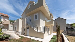 Ein modernes, zweistöckiges Haus mit Balkon, Treppe und kleinem Garten.