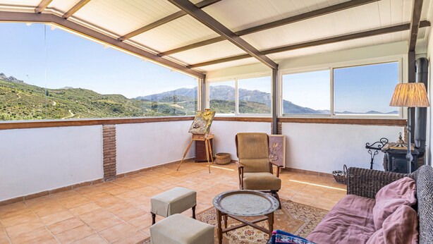 A balcony with a view of a mountainous landscape, a painting on an easel, a chair, a small table, and a sofa. - Stunning home in Periana (Periana)