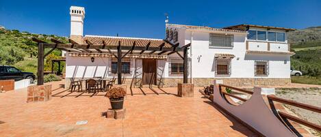 A white villa with a tiled patio, a pergola, and a view of the countryside.
