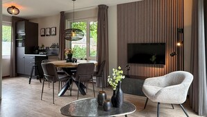 Un salon moderne comprenant un coin repas, une cuisine et un téléviseur fixé sur un mur à rayures.